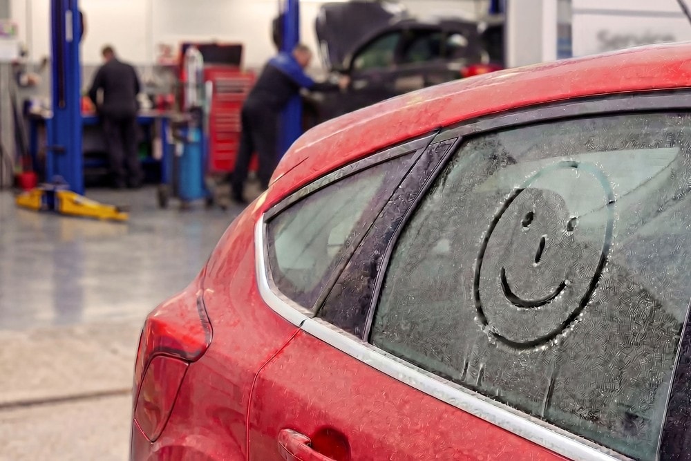 Punainen auto, jonka takalasin kuuraan on piirretty hymiö, pysäköitynä Fordin autokorjaamon sisälle.
