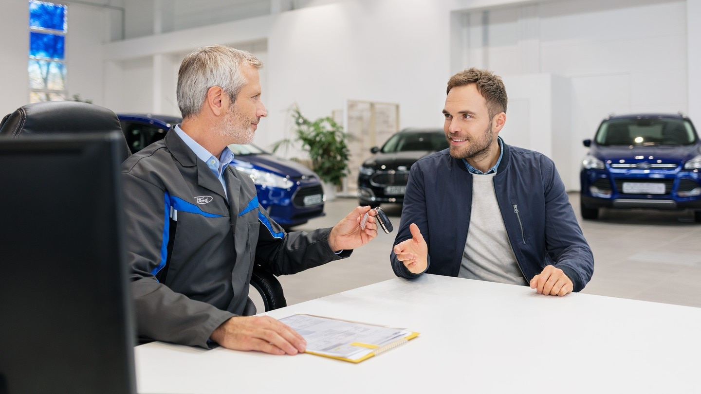 Ford-myyjä ojentaa avaimia iloiselle asiakkaalle