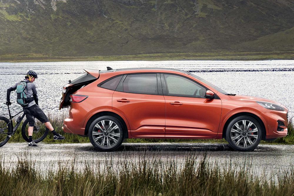 Oranssi Ford Kuga, jonka avoimeen tavaratilaan lastataan polkupyörää. Henkilö seisoo pyörän vieressä.