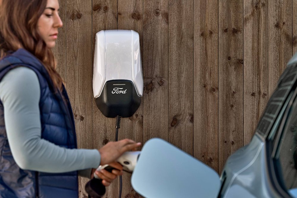 Nainen kytkee sinisen Ford Explorer -sähköautonsa kotilatausasemaan.