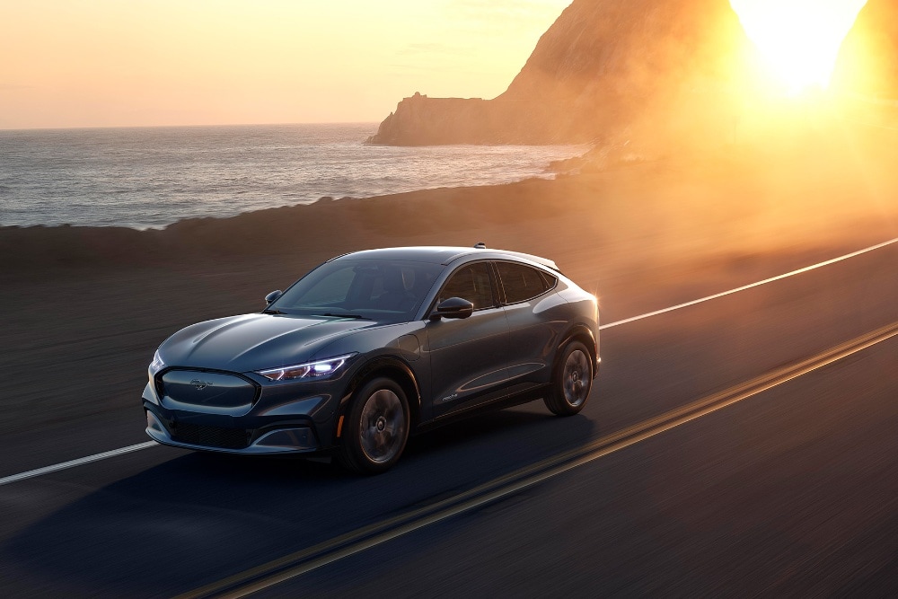 Täyssähköinen Ford Mustang Mach-E ajaa rannikkotiellä auringonlaskun aikaan.