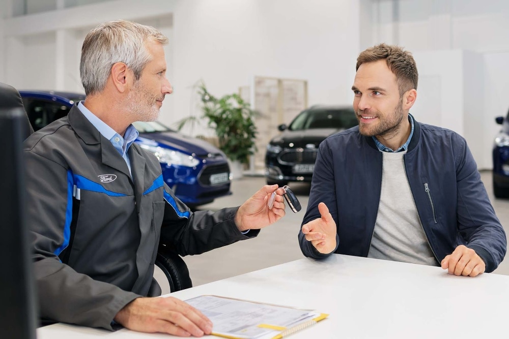Kaksi miestä istuu vastakkain Ford-jälleenmyyjällä.