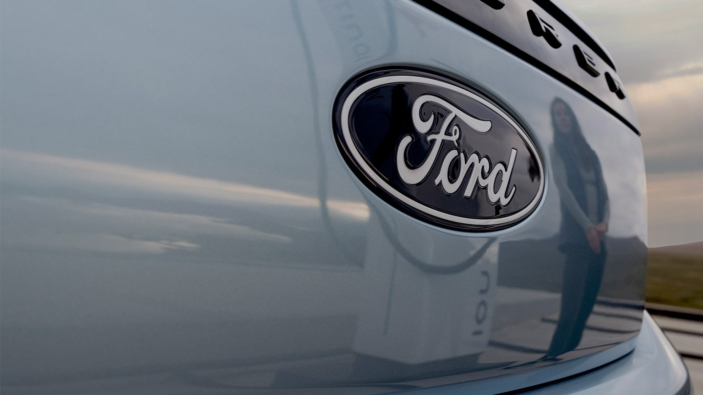 Täyssähköisen Ford Explorerin etuosan Ford-logo ja julkinen latausasema heijastuneena autoon.