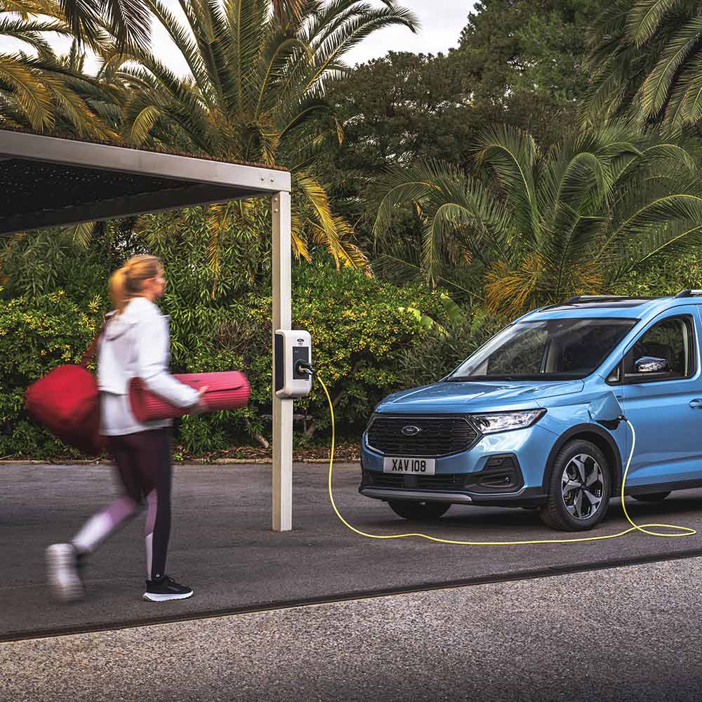 Henkilö kävelemässä jooga-matto kainalossa kohti Tourneo Connect ladattava hybridiä.