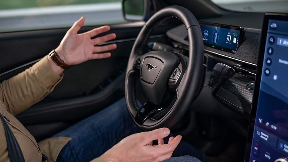 Mies istuu Ford Mustang Mach-E:ssä kädet irrotettuna ohjauspyörästä, mikä havainnollistaa BlueCruise-teknologiaa.