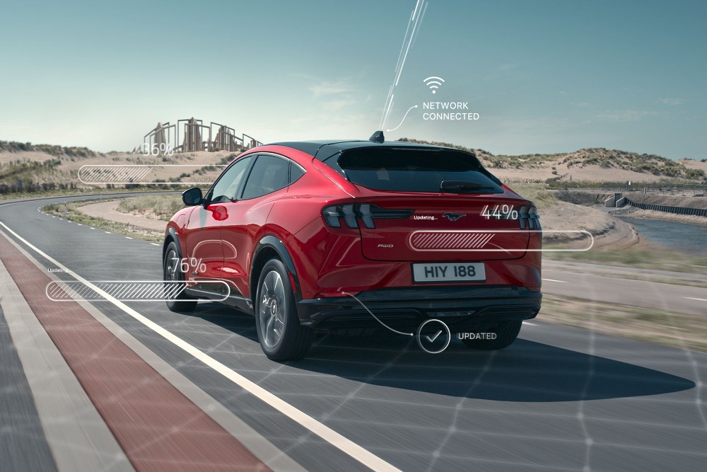 Rear view of a red Ford Mustang Mach-e driving along a road with connectivity diagrams coming off the vehicle