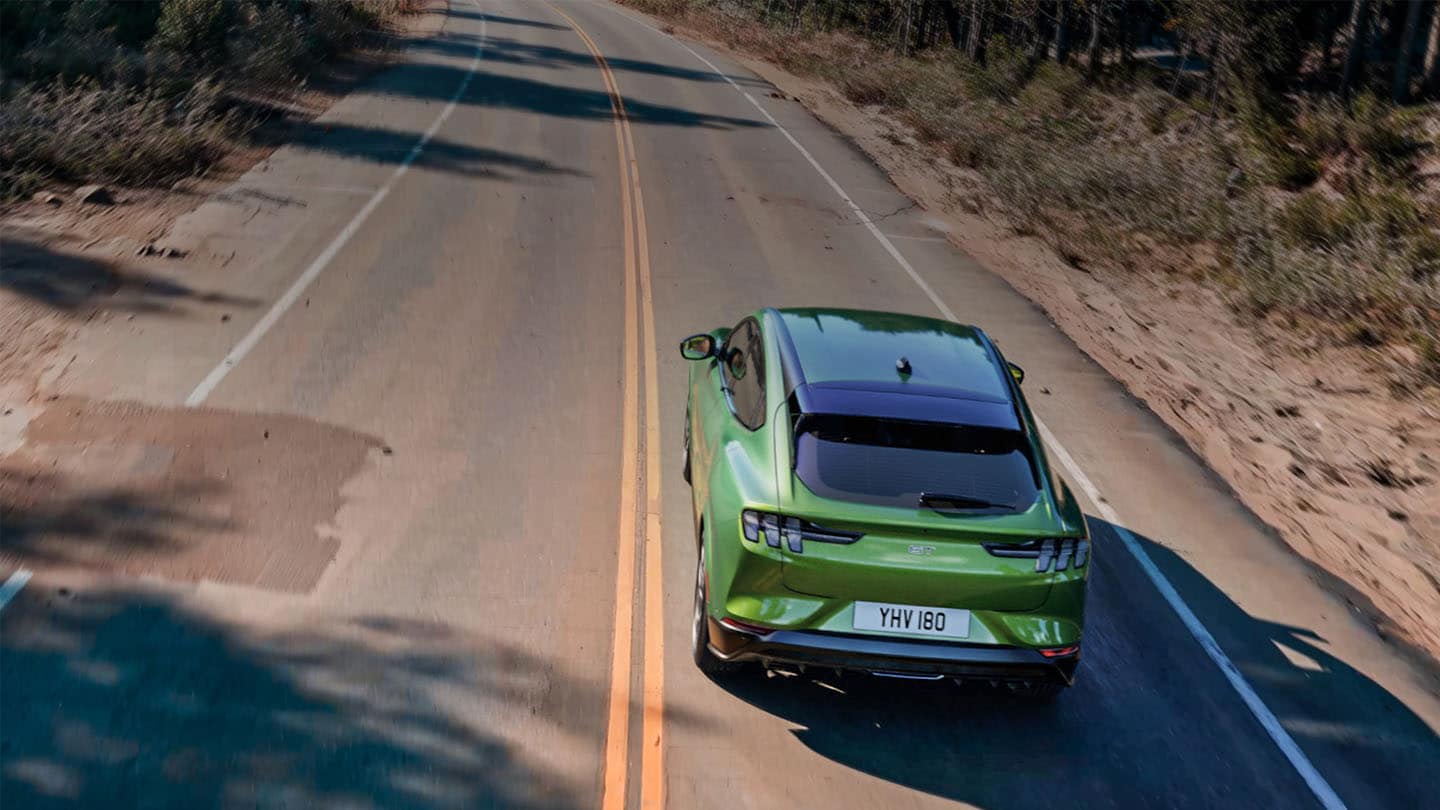 Eruption Green -värinen Ford Mustang Mach-E GT ajamassa puiden reunustamalla vuoristotiellä.