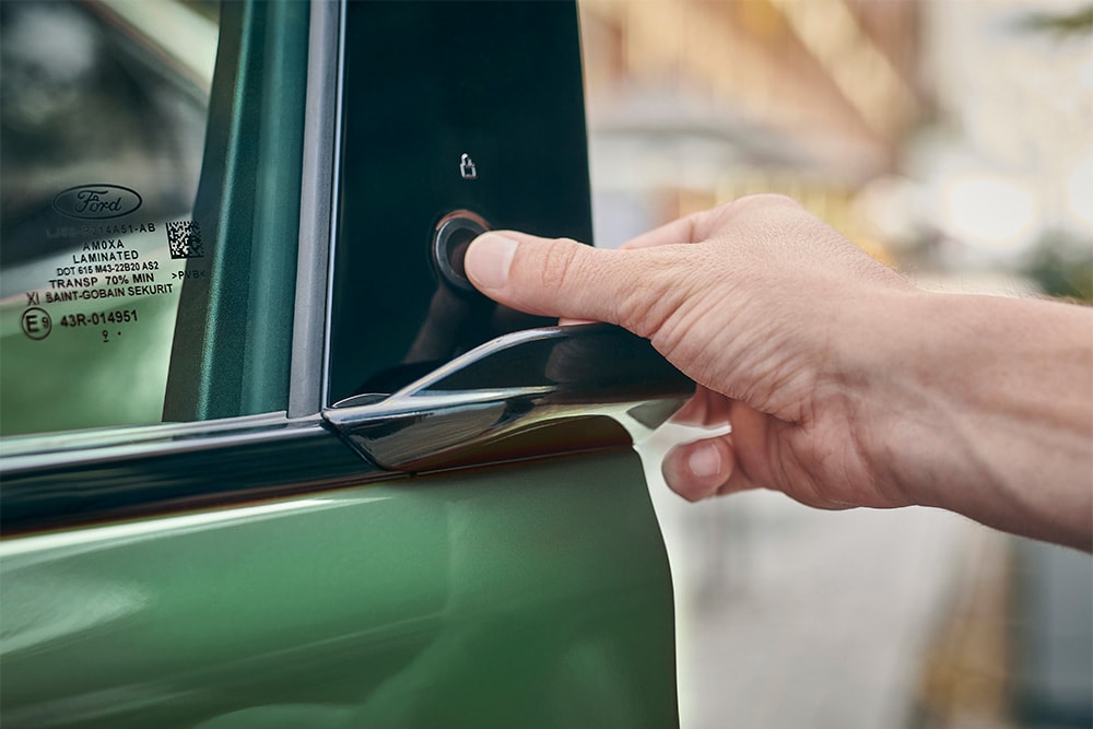 Lähikuva kädestä käyttämässä E-Latch-järjestelmää painamalla vihreän Ford Mustang Mach-E:n ovessa olevaa painiketta.