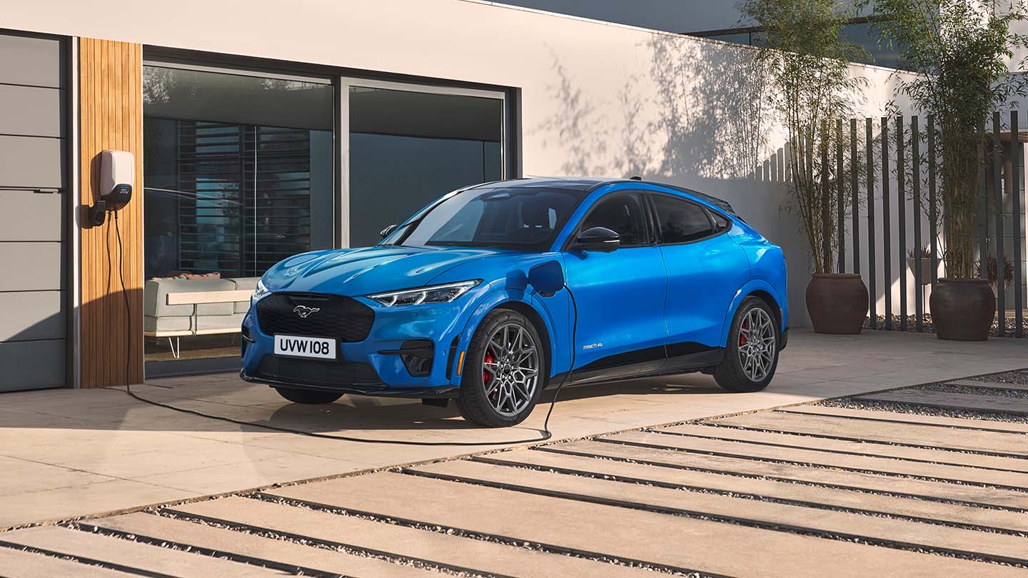 Sininen sähköinen Ford Mustang Mach-E kytkettynä kotilaturiin modernin talon edessä.