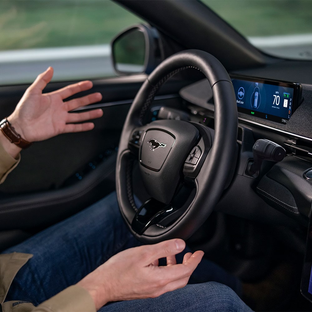 Kaksi kättä ohjauspyörän tuntumassa Mustang Mach‑E:ssä, esittelemässä BlueCruise‑automaattiajoa