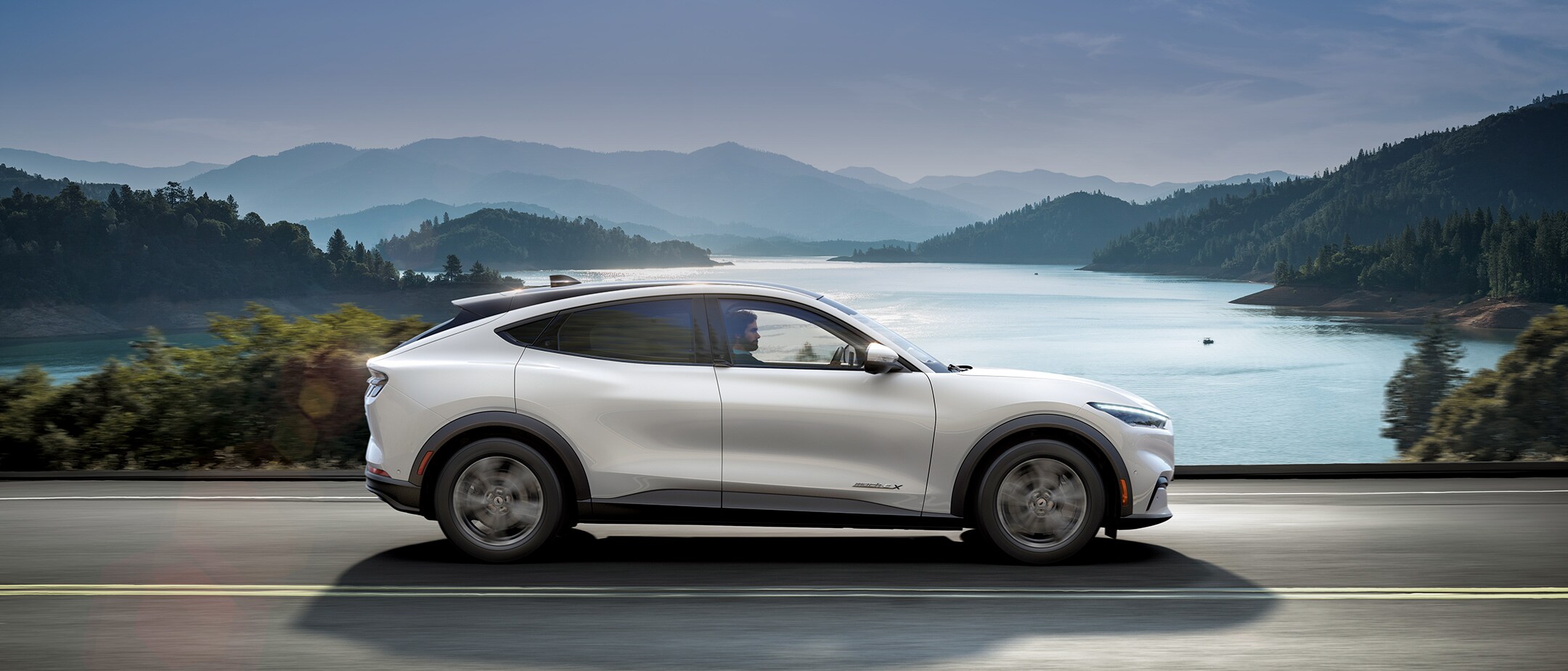 Silver All Electric Ford Mustang Mach-E driving sunny cliffs and sea