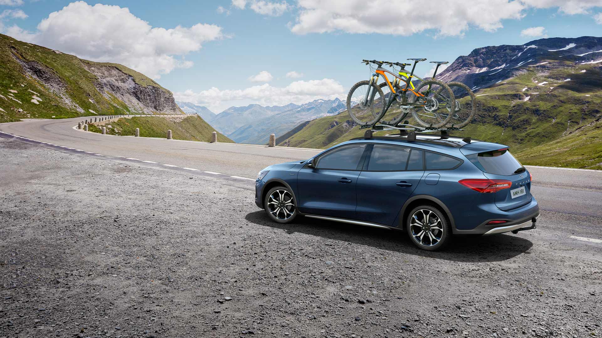 Sininen Ford Focus ajaa kauniilla vuoristotiellä polkupyörät kattoon kiinnitettyinä.