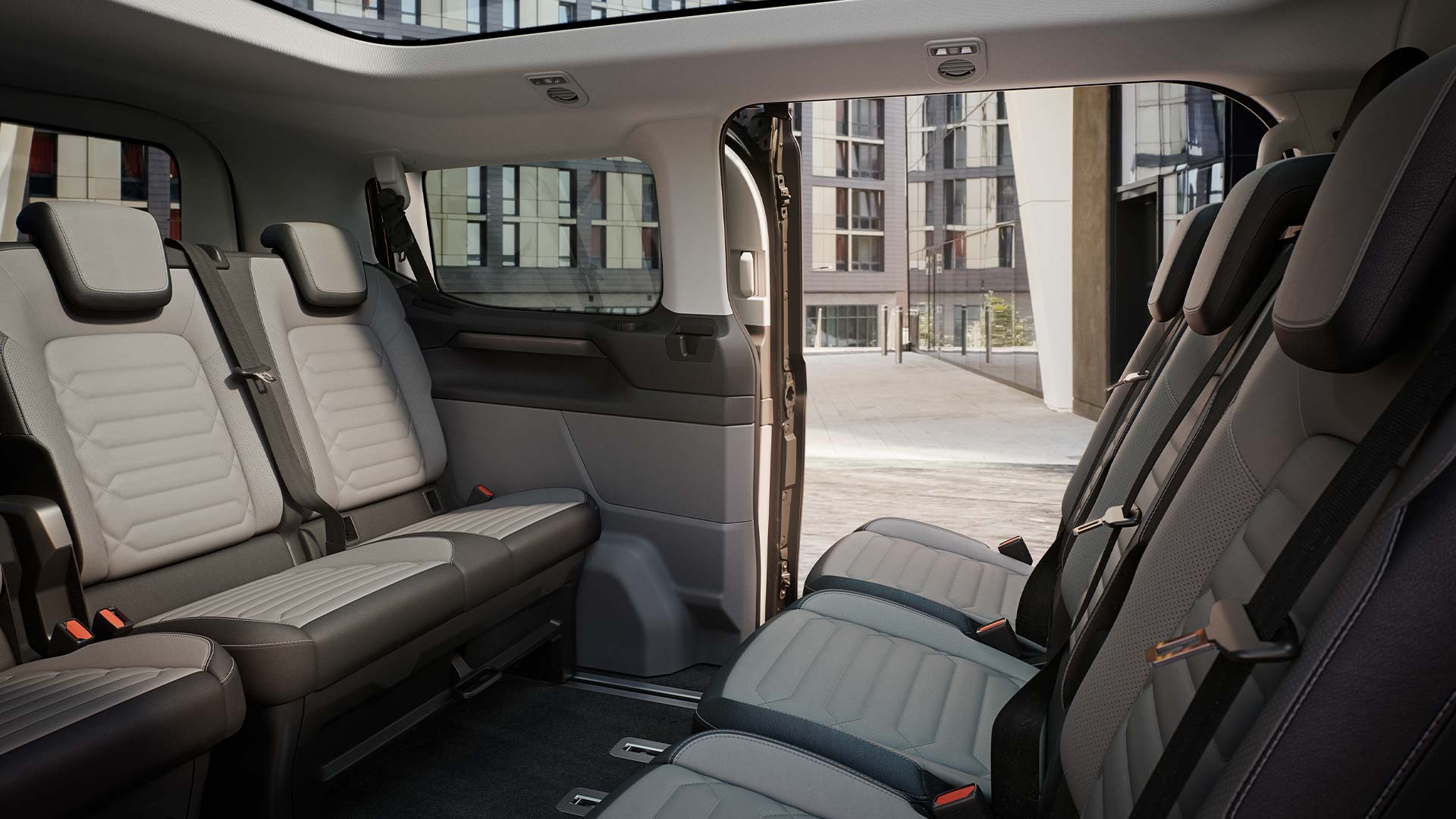 Ford Tourneo Customin sisätilat; kuvassa näkyy useita istuinrivejä harmaalla verhoilulla sekä panoraamakatto.