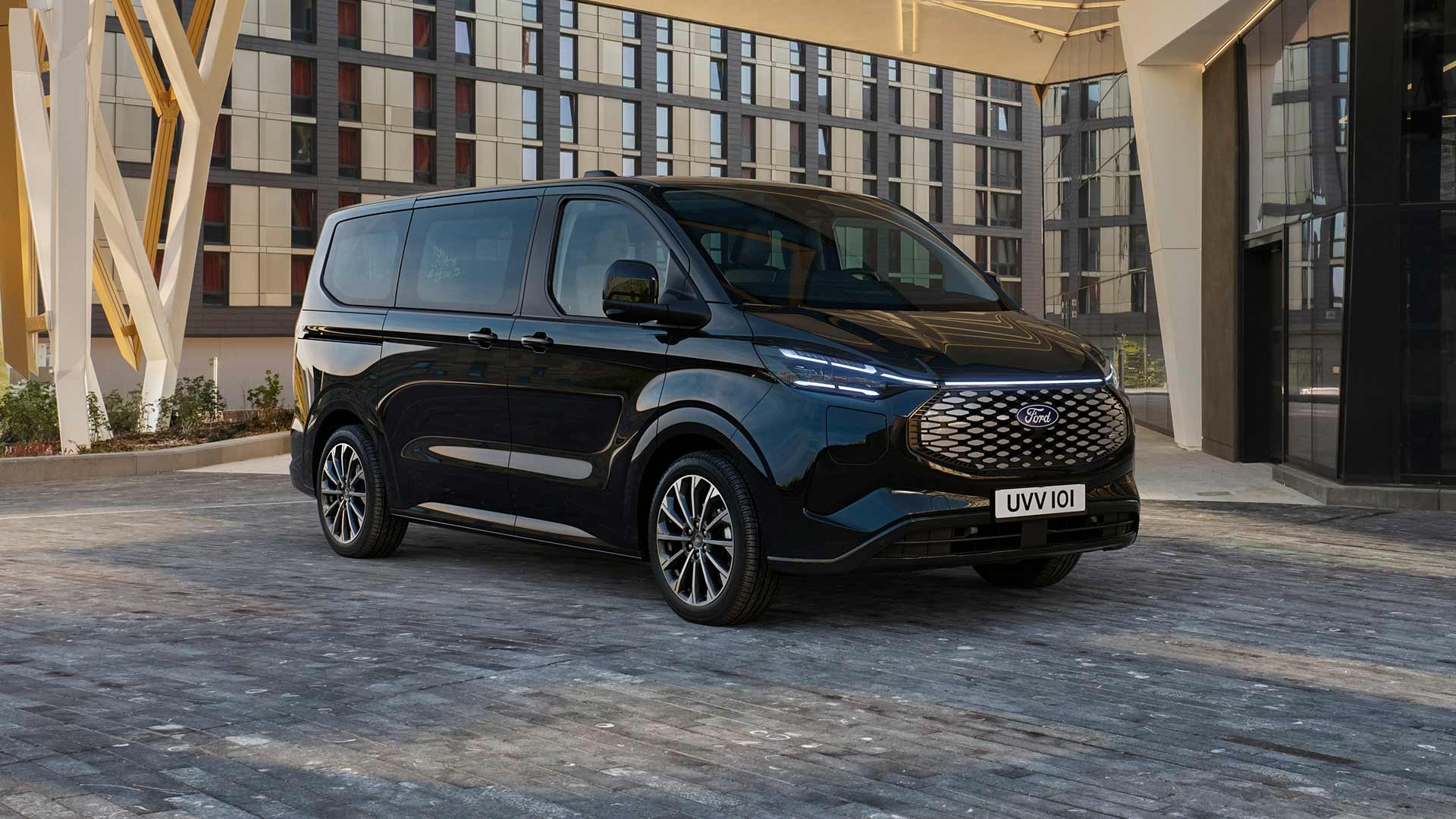 Musta Ford E-Tourneo Custom pysäköitynä modernin rakennuksen eteen.