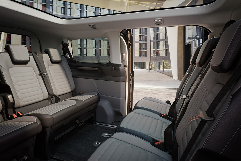 Ford Tourneo Customin sisätilat; kuvassa näkyy useita istuinrivejä harmaalla verhoilulla sekä panoraamakatto.