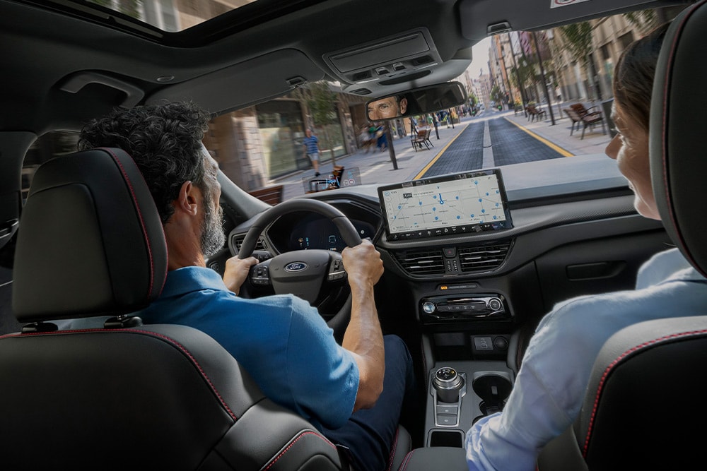 Kaksi ihmistä  Ford Kuga -autossa ajamassa kaupungissa 12,3 tuuman digitaalinäytön ohjeita seuraten.