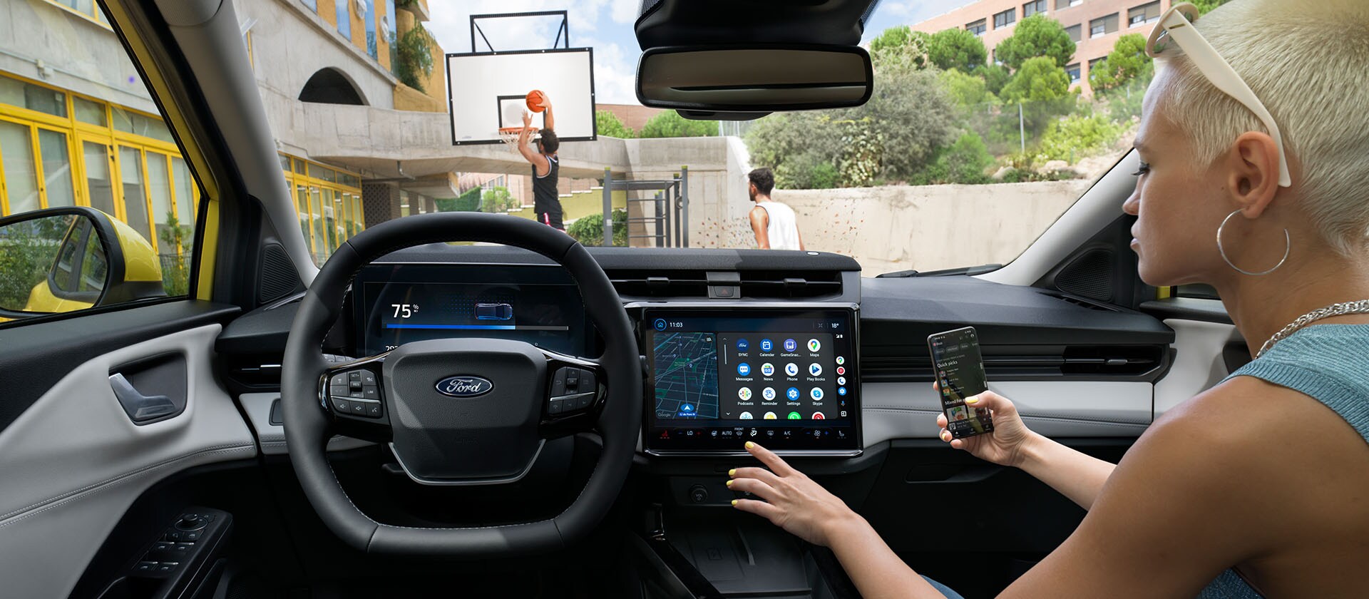 Sähköisen Ford Puma Gen-E:n® sisätilat ja henkilö, joka synkronoi puhelintaan suuren kosketusnäytön kanssa.
