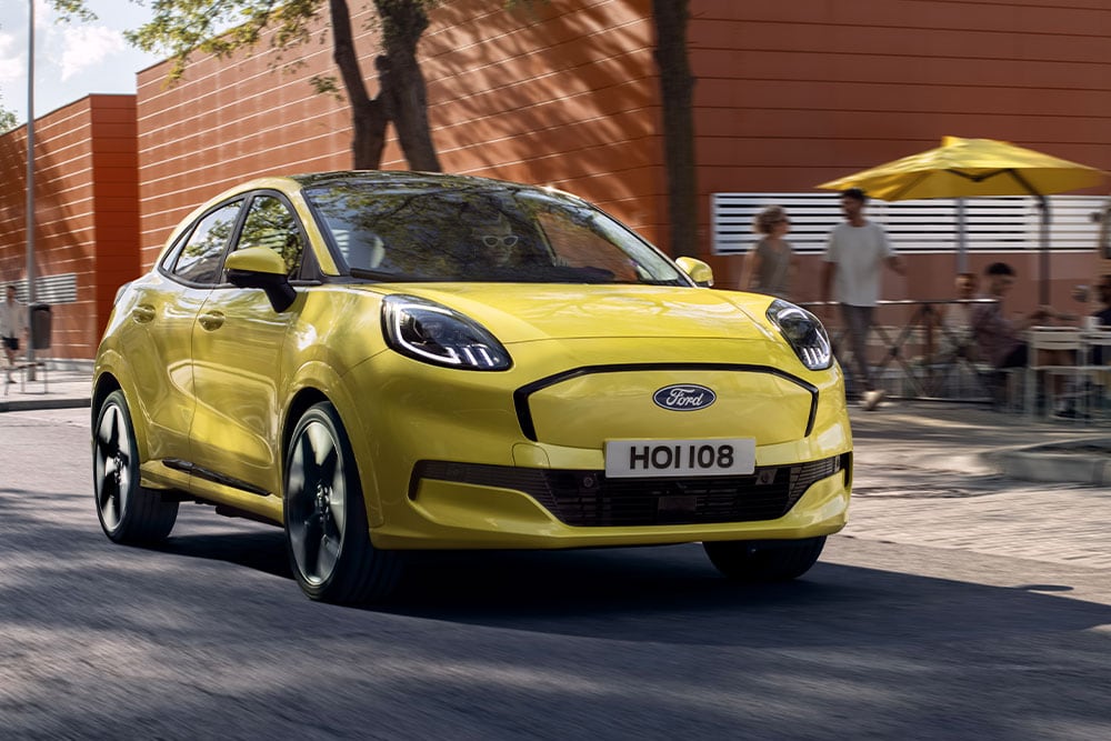 Keltainen sähköinen Ford Puma Gen-E® edestä kuvattuna ajamassa kaupungin kadulla.