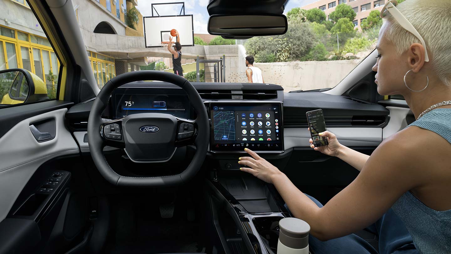 Sähköisen Ford Puma Gen-E:n® sisätilat ja henkilö, joka synkronoi puhelintaan suuren kosketusnäytön kanssa.
