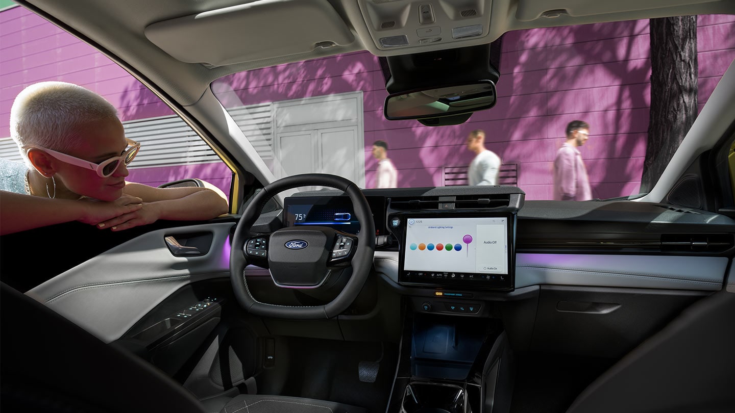Henkilö katselee uuden Ford Puma Gen-E:n® sisätiloja, joissa on suuri kosketusnäyttö ja tunnelmavalaistus.