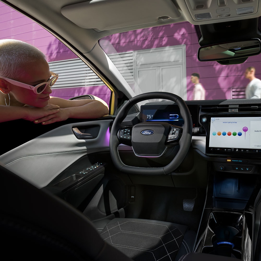 Sähköisen Ford Puma Gen-E:n® sisätilat ja henkilö, joka katselee suurta tietoviihdejärjestelmän näyttöä ikkunan läpi.