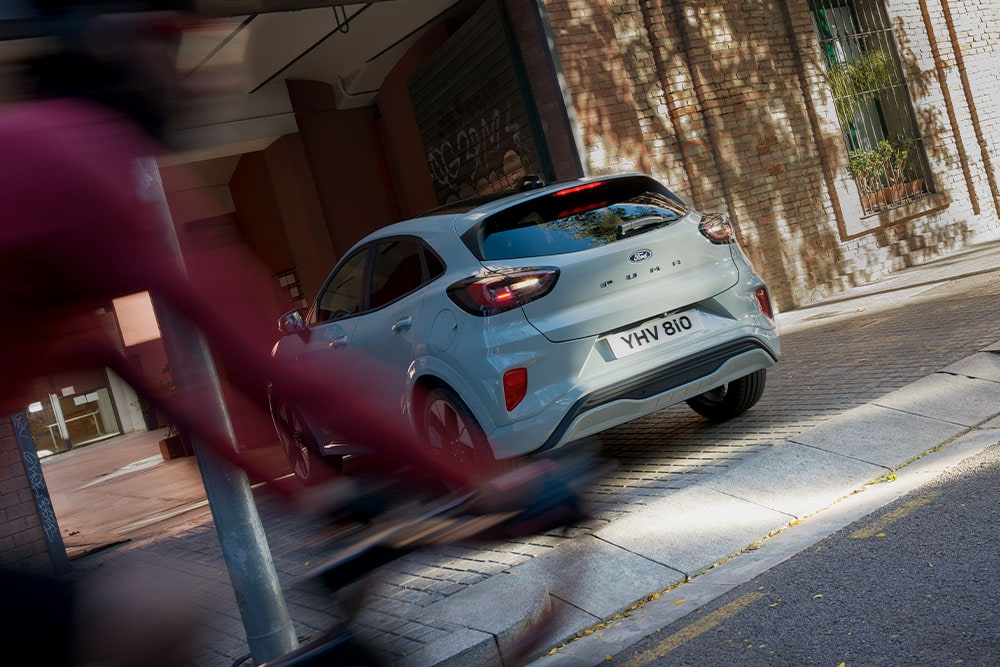 Takaa kuvattu harmaa Ford Puma pysäköitynä vehreälle kaupungin kadulle.