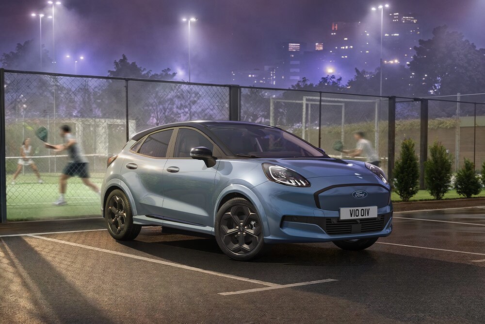 Sininen Ford Puma Gen-E pysäköitynä tenniskentän viereen, taustalla kaupungin valot.