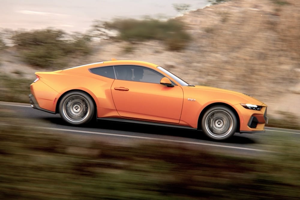 Sivu­kuva Ford Mustang GT Fastbackista Orange Fury -värissä ajamassa tietä pitkin