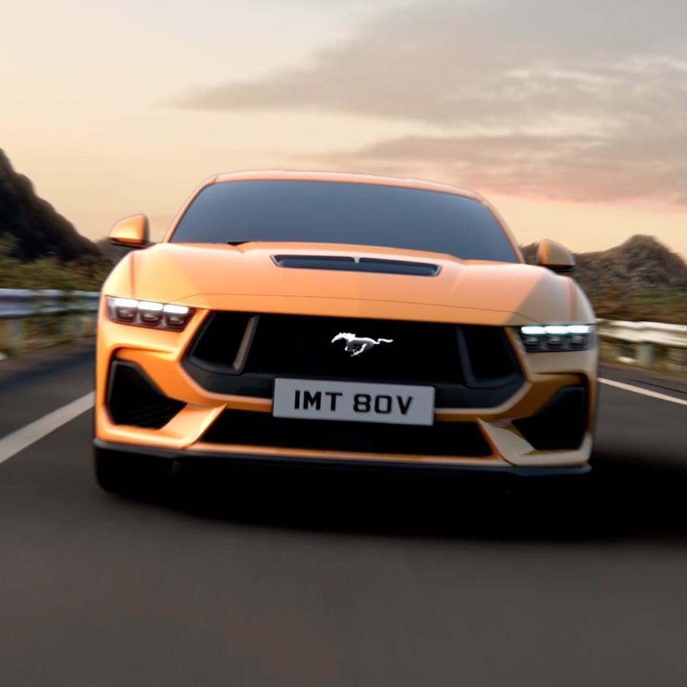 Edestä otettu kuva oranssista Ford Mustangista, lähikuvassa ajovalot, etusäleikkö ja Mustang-merkki