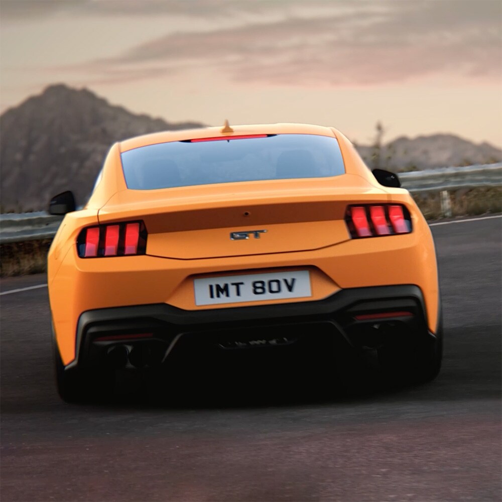 Ford Mustang GT Fastback Orange Fury -värissä ajamassa tiukkaa mutkaa maantiellä