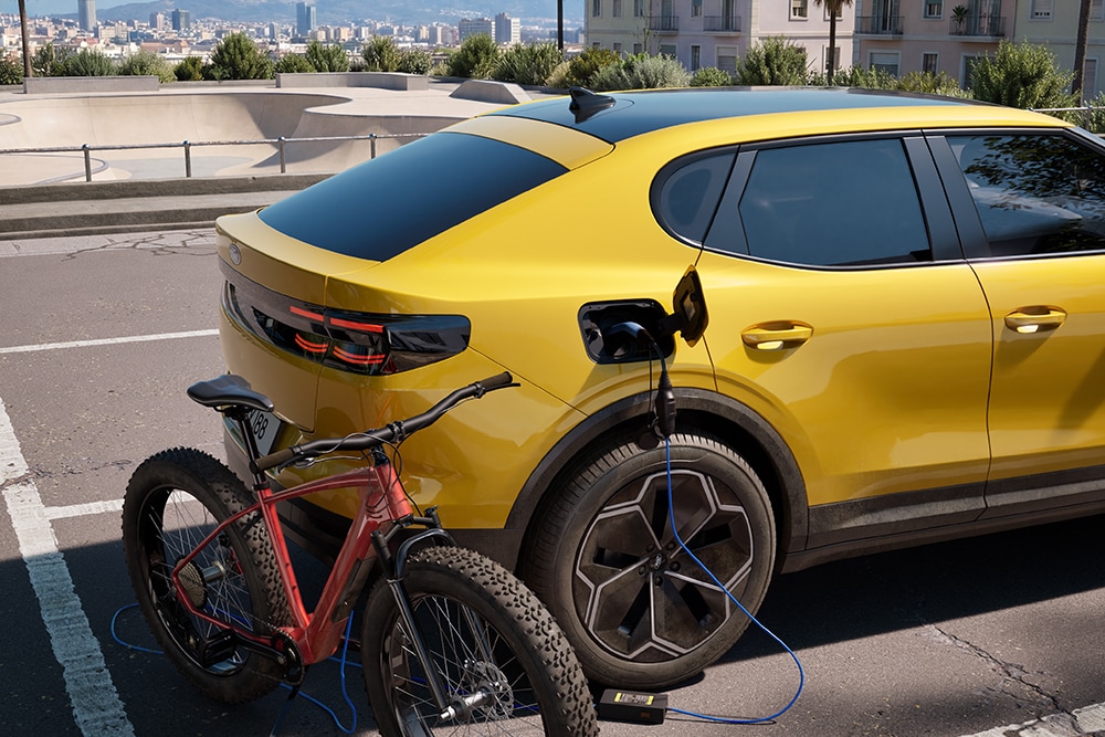Keltainen Ford Capri® pysäköitynä. Samalla lataa punaista sähköpyörää kaupunkiympäristössä.
