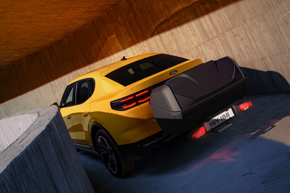 Moderniin betonirakenteeseen pysäköity keltainen Ford Capri, telineelle taakse on kiinnitetty kuljetuslaatikko