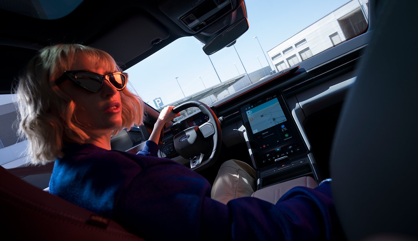 Nainen istuu Ford Caprin kuljettajan paikalla. Kuvassa näkyy ohjauspyörä ja suuri SYNC® Move -kosketusnäyttö.