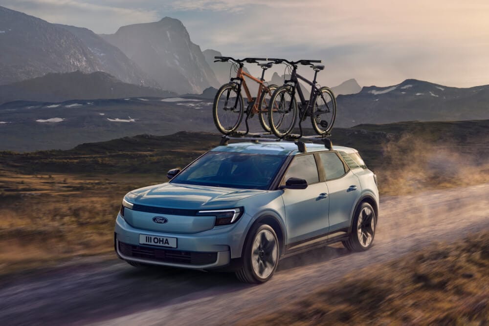 Sininen Ford Explorer ajaa hiekkatiellä, taakkateline, kattopyöräteline ja kaksi polkupyörää asennettuna katolle.