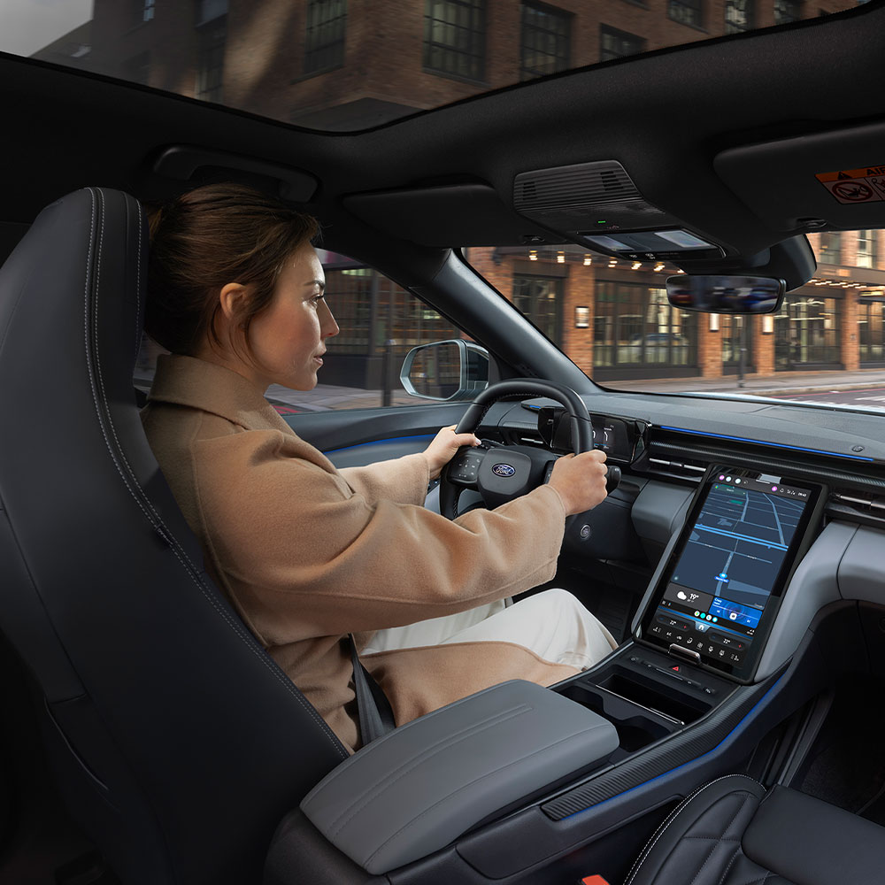 Henkilö ajaa täyssähköisellä Ford Explorerilla kaupungin läpi, näkyvillä suuri 14,6-tuumainen SYNC Move -kosketusnäyttö.