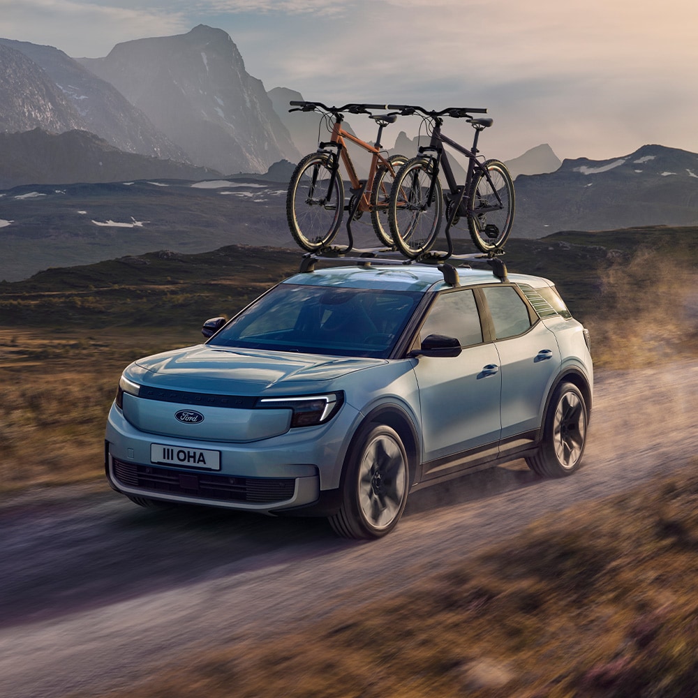 Sininen Ford Explorer ajaa hiekkatiellä, taakkateline, kattopyöräteline ja kaksi polkupyörää asennettuna katolle.