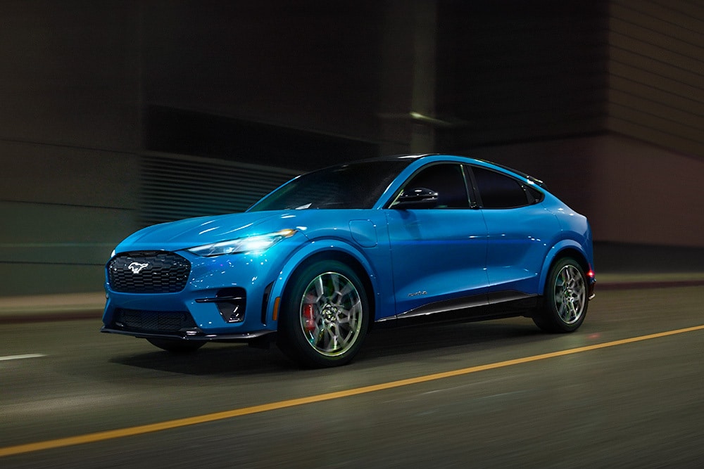 Sininen sähköinen Ford Mustang Mach-E GT -urheiluauto ajamassa avoimella tiellä.