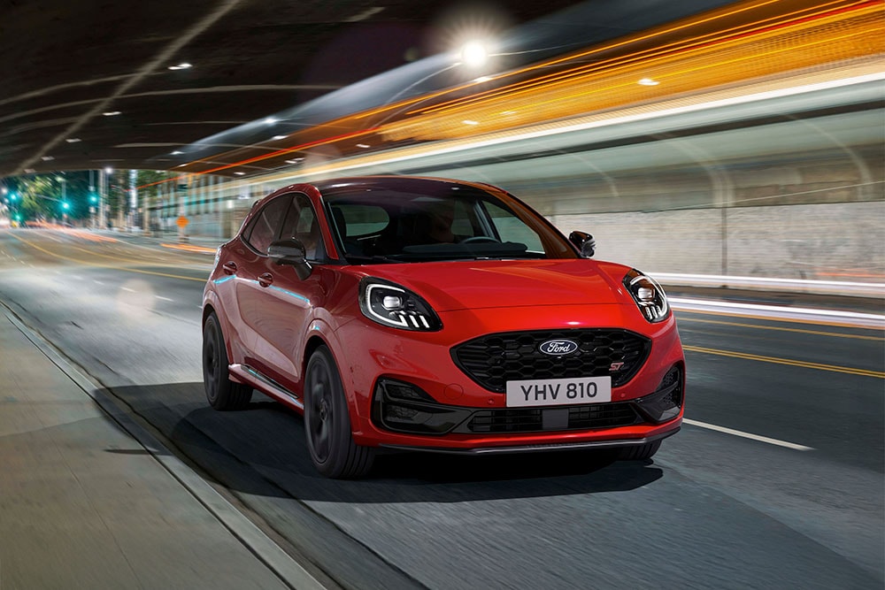 Punainen urheilullinen Ford Puma ST -katumaasturi ajamassa kirkkaasti valaistulla öisellä kaupungin kadulla.