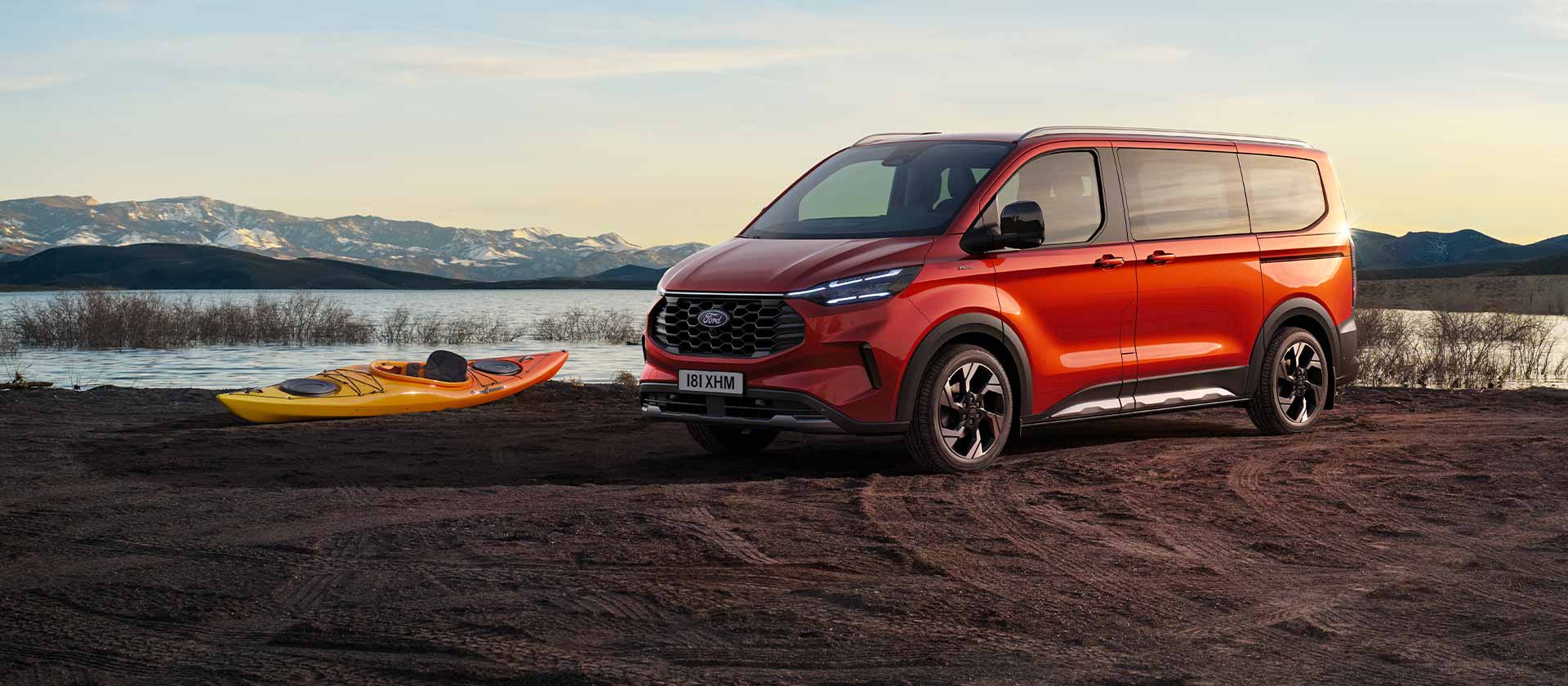Punainen Ford Tourneo Custom -pakettiauto pysäköitynä lähelle järveä kajakin kanssa. 