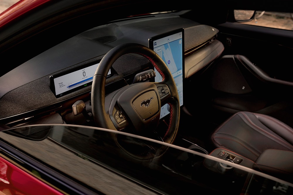 Ford Mustang Mach-E:n sisätilat, joissa näkyvät ohjauspyörä, digitaalinen mittaristo ja suuri keskusnäyttö.