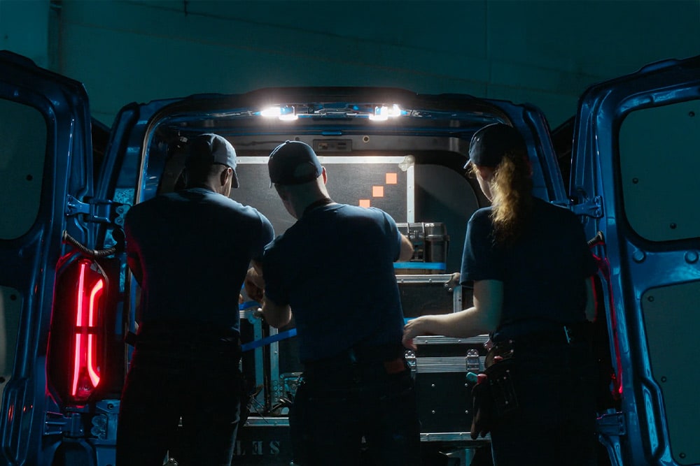 Kolme henkilöä työskentelemässä sähköisen Ford E-Transit Custom -pakettiauton takaosassa.