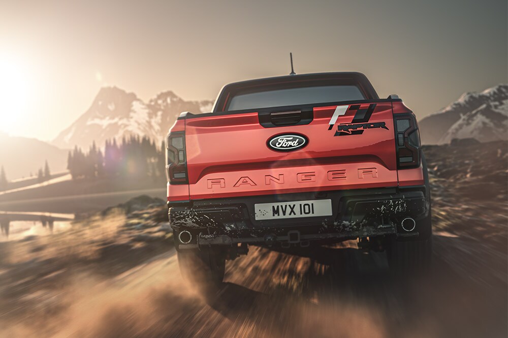 Takanäkymä punaisesta Ford Ranger Raptorista ajamassa soratiellä, ja taustalla kohoaa vuoria.