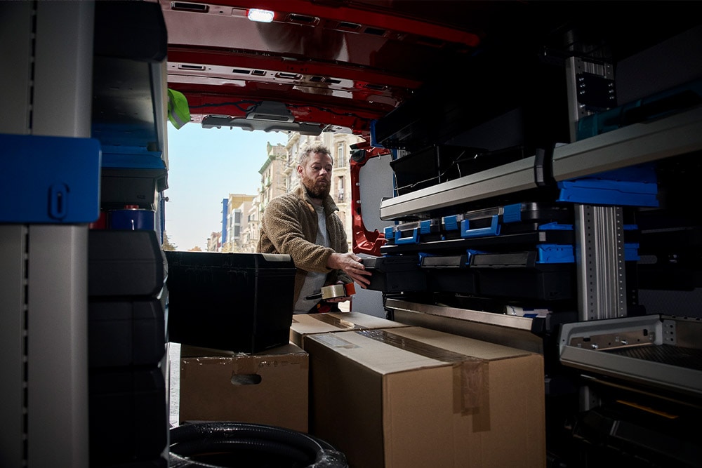 Kuljetusyrityksen työntekijä purkaa paketteja punaisesta Ford Transit Customista.