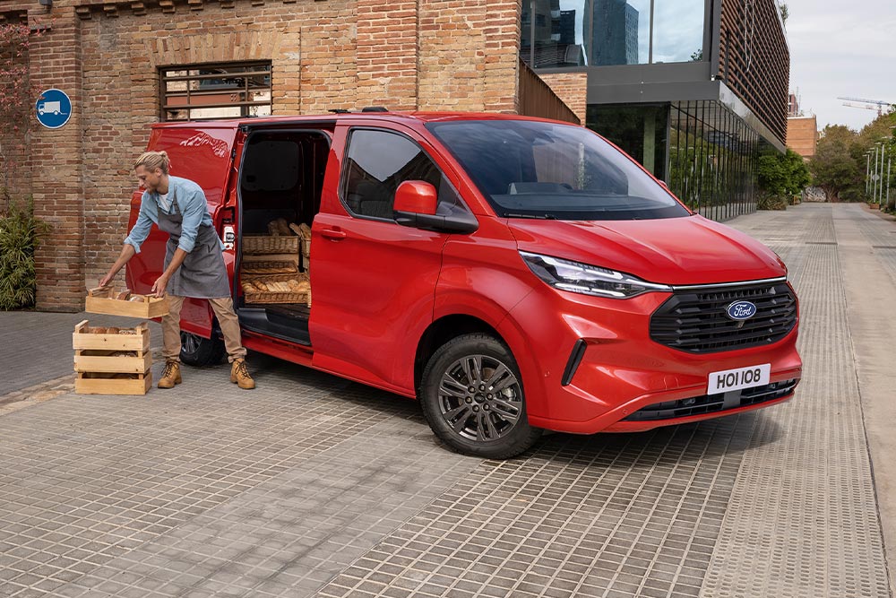 Kuljetusyrityksen kuljettaja lastaamassa paketteja punaiseen Ford Transit Customiin.