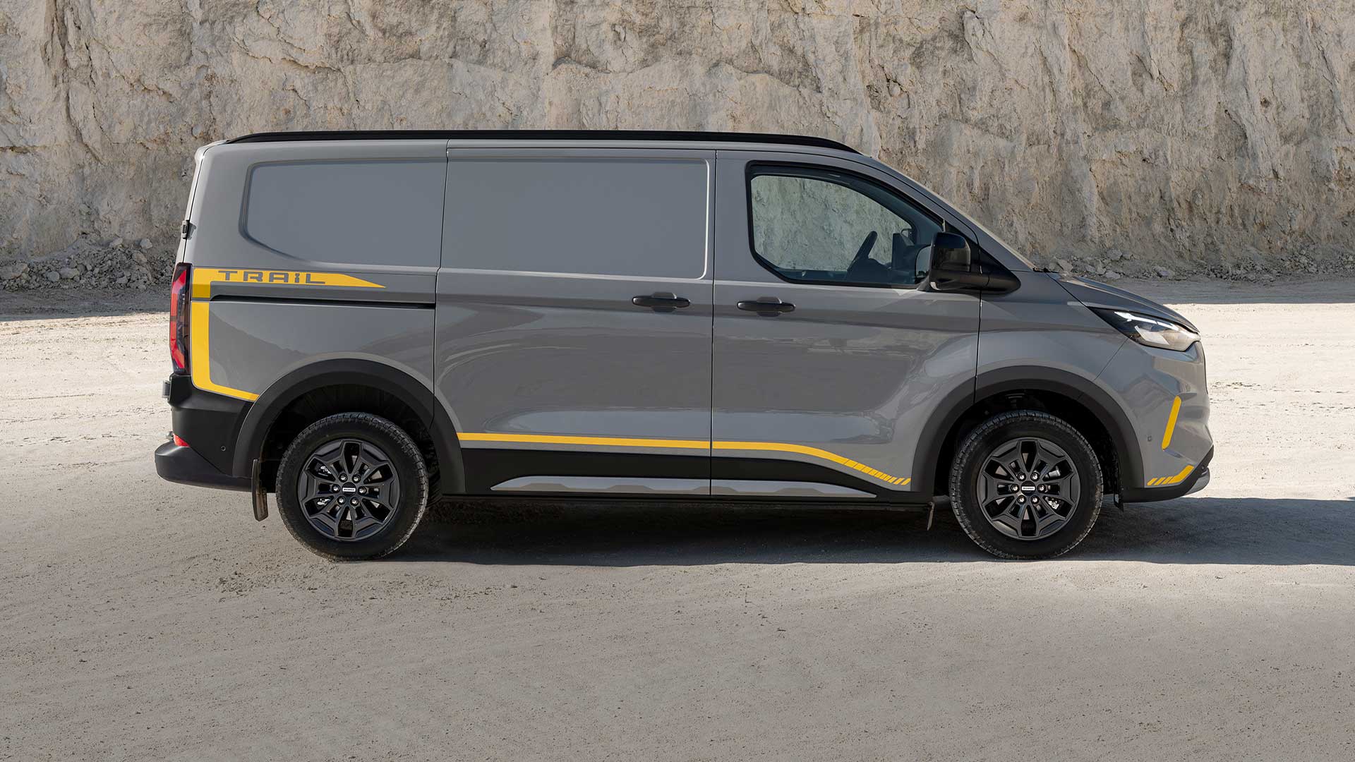 Harmaa Ford Transit Custom Trail -pakettiauto keltaisilla yksityiskohdilla sivusta kuvattuna.