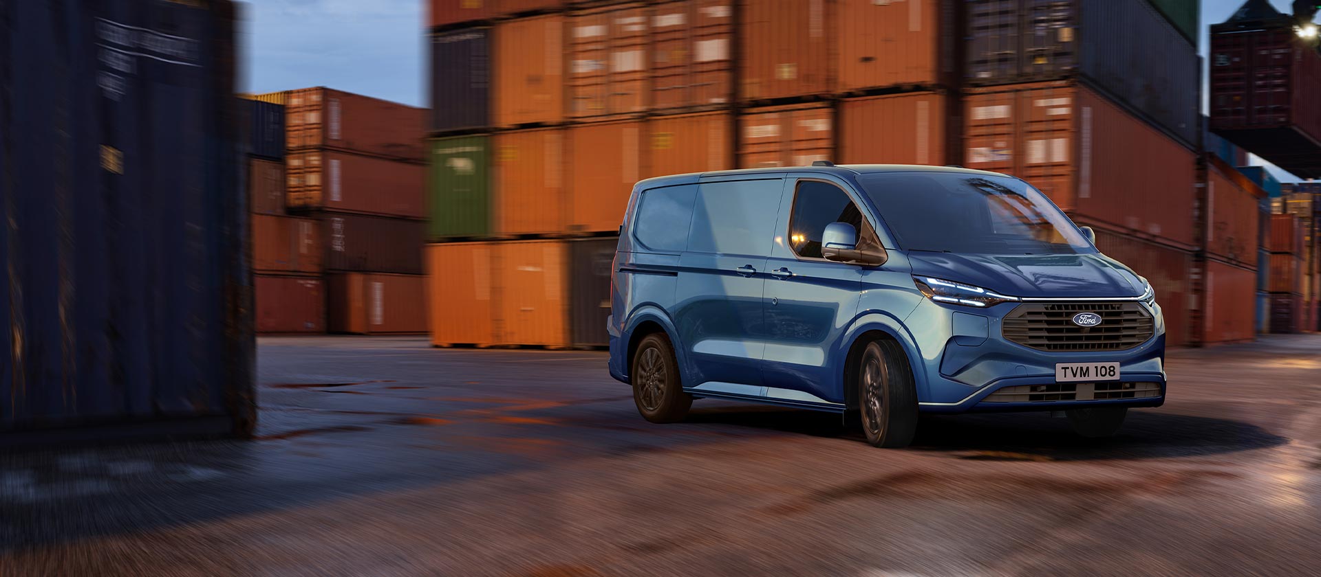 Sininen Ford Transit Custom ladattava hybridi -pakettiauto ajamassa satama-alueella.