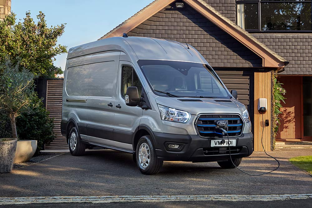 Talon viereen ajotielle pysäköity hopeanvärinen Ford E-Transit -pakettiauto yhdistettynä latausasemaan.