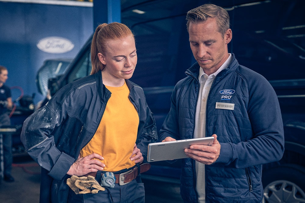 Kaksi mekaanikkoa korjaamolla katsomassa tablettia Ford E-Transit -sähköpakettiauton edessä.