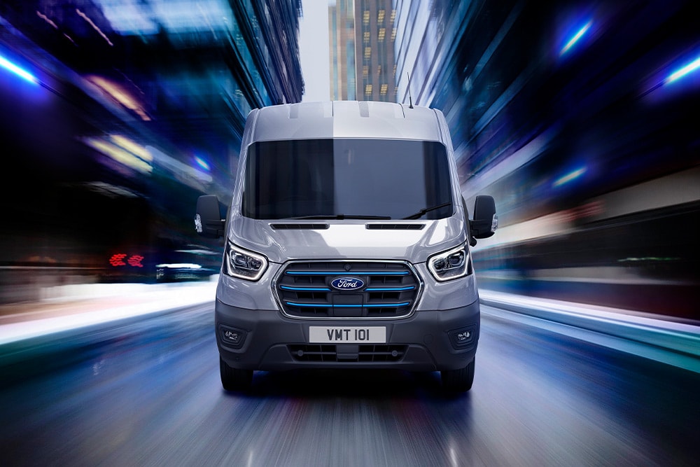 Tummanharmaa Ford E-Transit -sähköpakettiauto ajamassa tiellä.