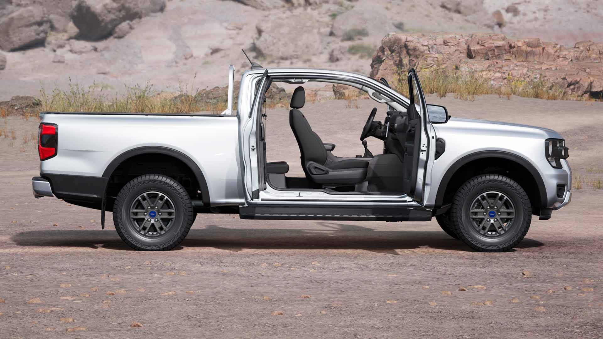 Profiilinäkymä hopeanharmaasta ovet auki olevasta Ford Ranger XLT Super Cabista, joka on pysäköity pölyiseen maastoon.